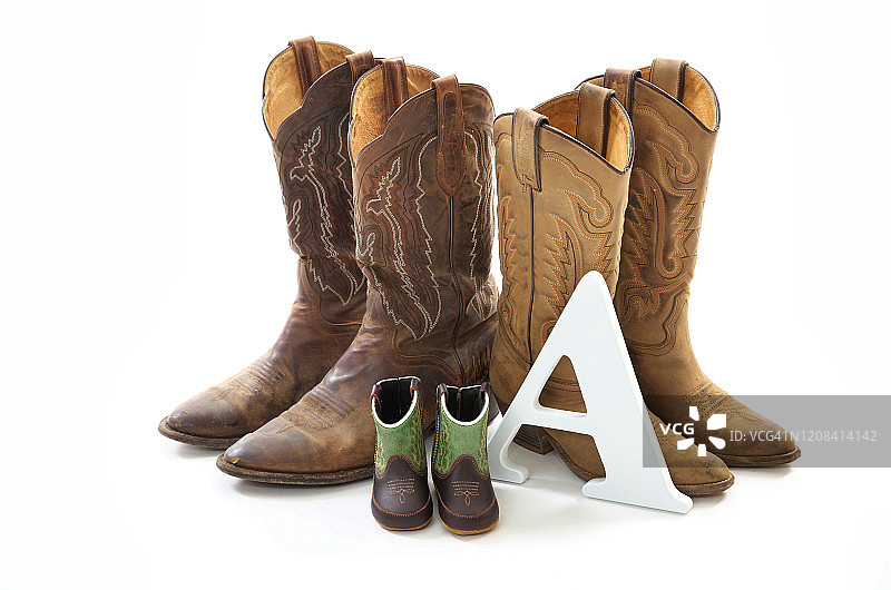 两双成人牛仔靴和一双婴儿或幼儿的超小牛仔靴特写，带有字母“A”图片素材