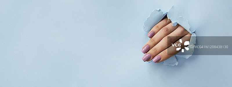 女性美甲从纸背景的孔中伸出图片素材