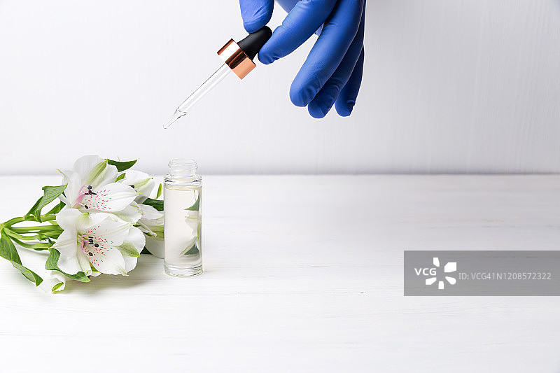 戴医用手套的手拿着滴管和美容精华液瓶。护肤美容产品概念图片素材