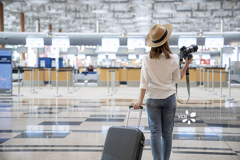 年轻女人戴着草帽，手持数码相机站在机场，旅行概念图片素材