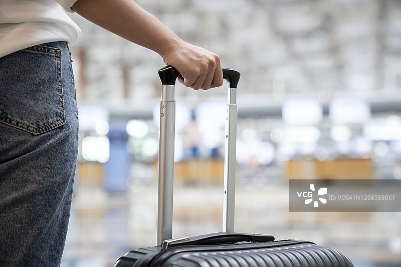 女人的手局部，手持行李站在航站楼内。图片素材