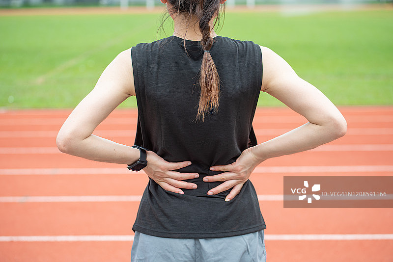 年轻跑步女性在体育场跑道上跑步后背痛或腰部酸痛的背影图片素材
