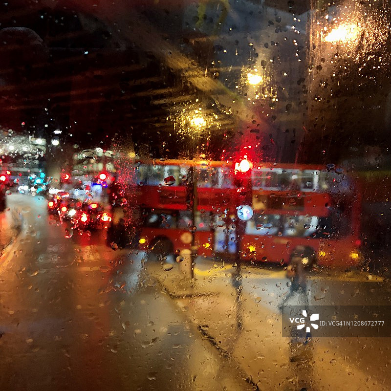 从巴士顶上俯瞰伦敦街道，冬日暴雨的夜晚灯光模糊了十字路口图片素材