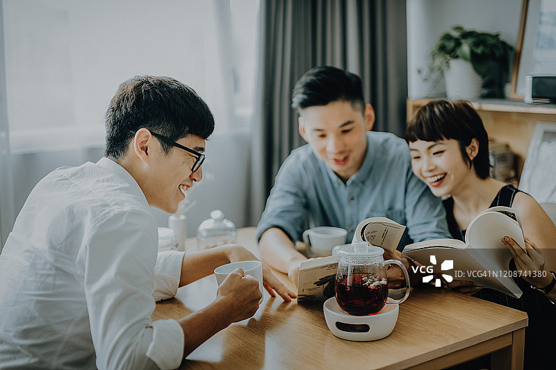 一群朋友在客厅里放松地喝咖啡和茶，愉快地聊天和读书图片素材