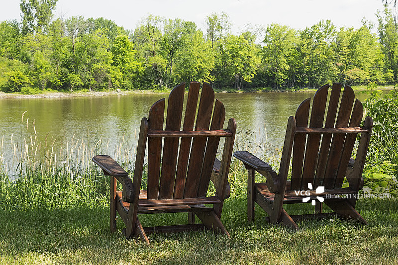 河边常绿树下的棕色木制阿迪朗达克椅图片素材