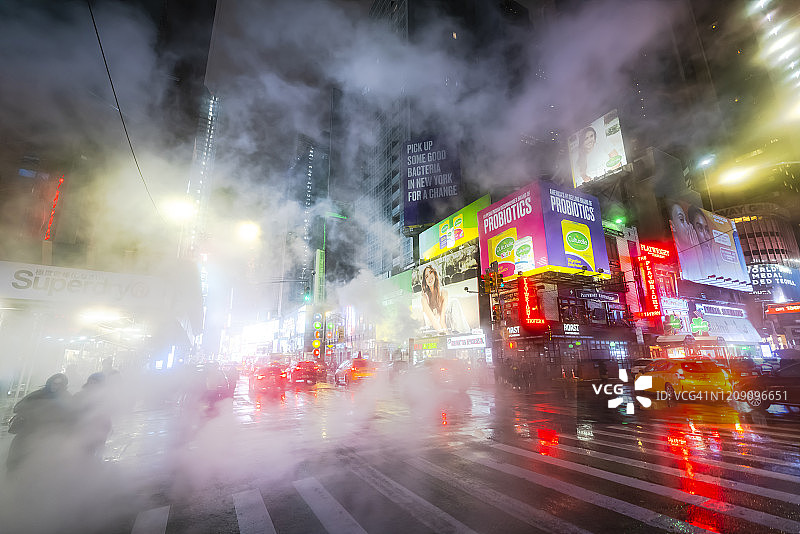 2020年1月18日，纽约市曼哈顿中城时代广场建筑群中，蒸汽升腾，在雪夜的十字路口弥漫，周围环绕着人群、交通和城市景观图片素材