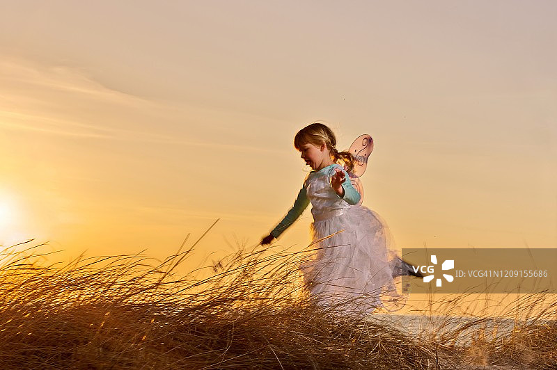 夕阳下，装扮成仙女的小女孩在海滩上奔跑图片素材