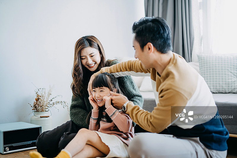 年轻家庭在家中享受欢乐时光，父亲开心地捏着女儿的脸颊图片素材