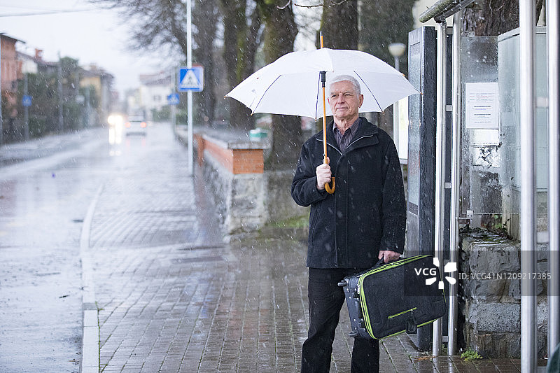在雨中公交车站等待的年长男性图片素材