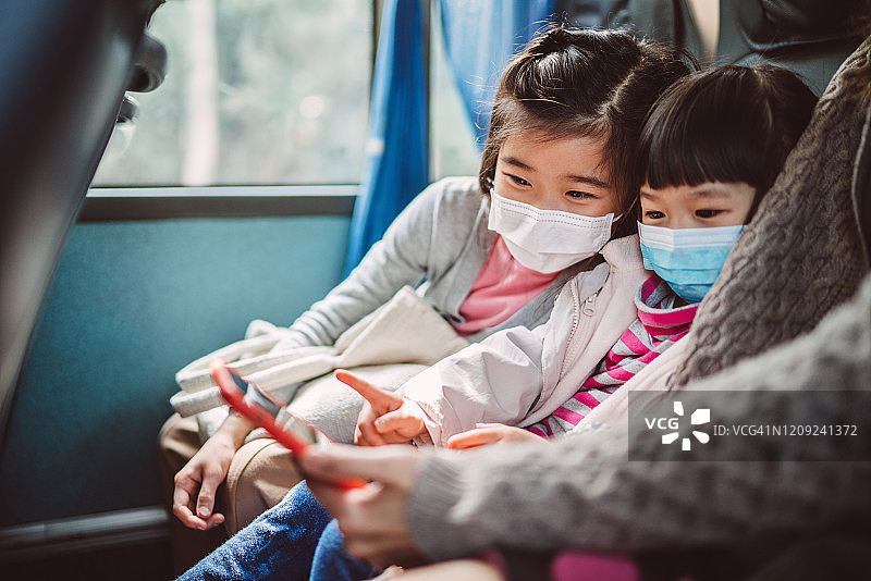 戴口罩的两姐妹和妈妈在公交车上使用智能手机图片素材