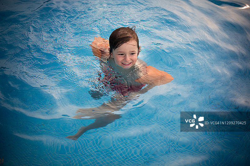 戴着充气袖套在泳池里的快乐男孩图片素材