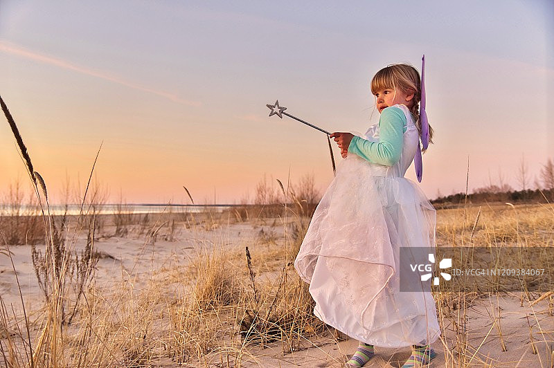 穿着仙女服装在海滩日落时分的可爱的年轻女孩肖像图片素材