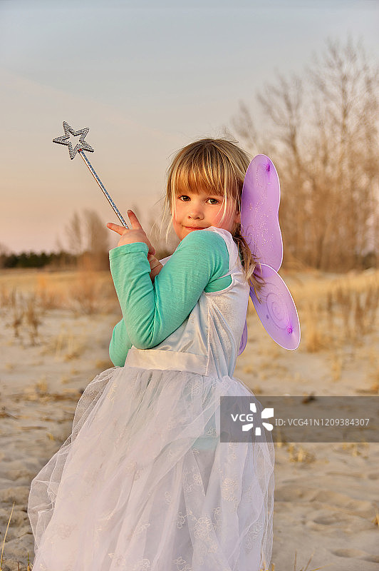 穿着仙女服装在海滩日落时分的可爱的年轻女孩肖像图片素材