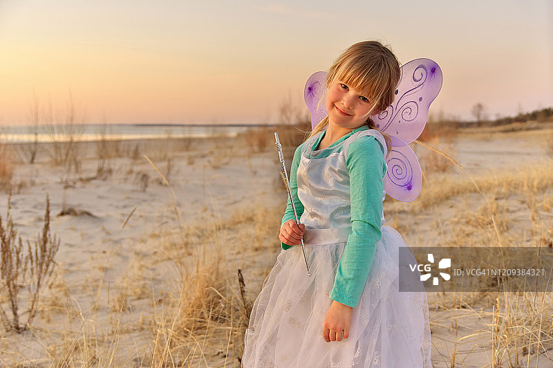 穿着仙女服装在海滩日落时分的可爱的年轻女孩肖像图片素材