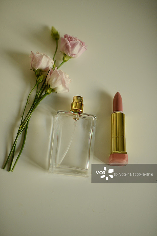白色背景上的两朵淡粉色玫瑰、香水瓶和裸色口红图片素材