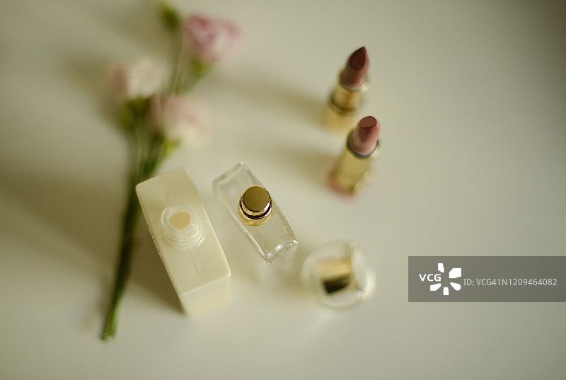 淡粉色玫瑰旁的乳液瓶、香水瓶和两支口红图片素材