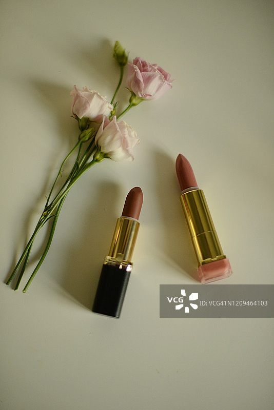 白色背景上的两支口红和三朵淡粉色玫瑰图片素材