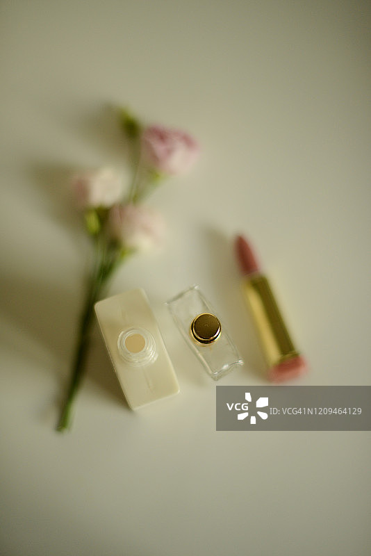 淡粉色玫瑰旁边的乳液瓶、香水瓶和裸色口红图片素材