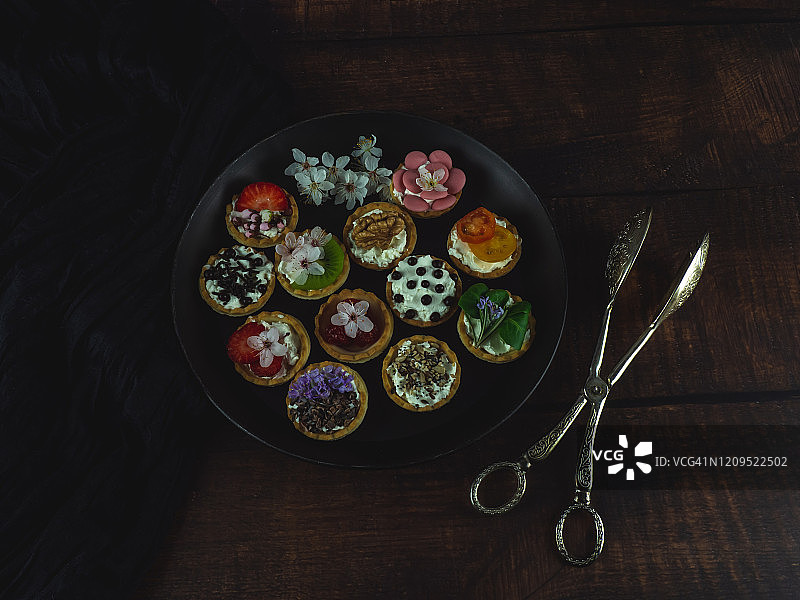 木桌上盛有甜咸味小点心和食用花的黑色圆盘图片素材