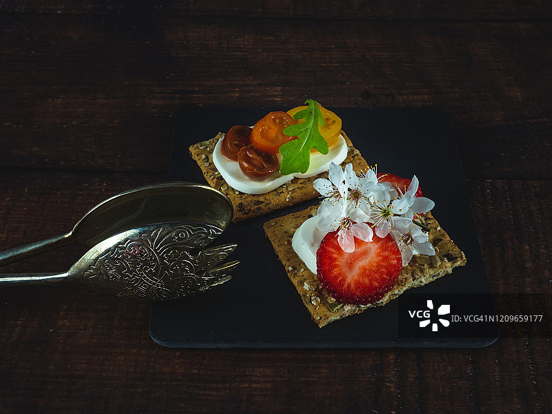 奶油奶酪草莓甜点和鲜奶酪樱桃番茄咸味小吃，芝麻饼干和木桌上的老羊驼肉钳图片素材