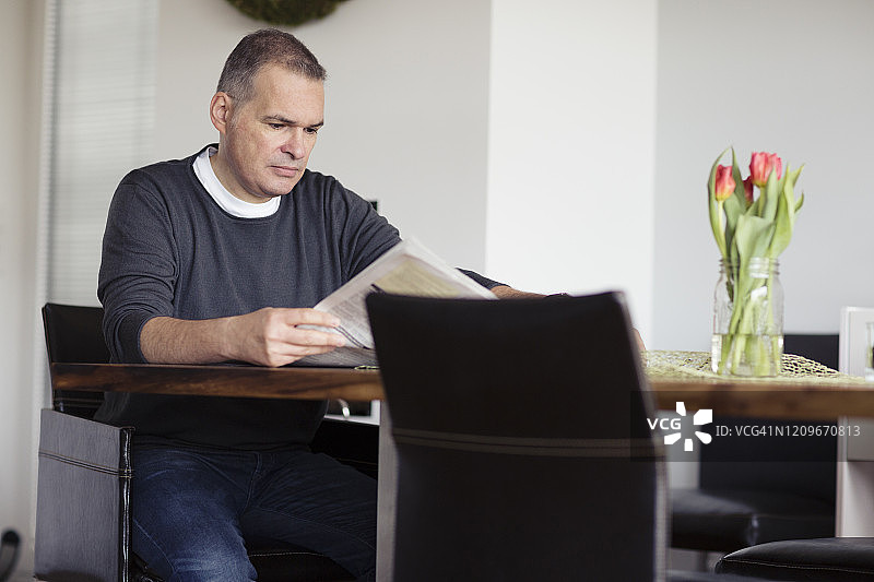 男子坐在餐桌旁阅读报纸图片素材