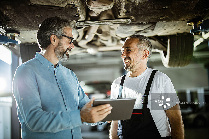 快乐的经理和汽车修理工在车间使用触控板交谈图片素材