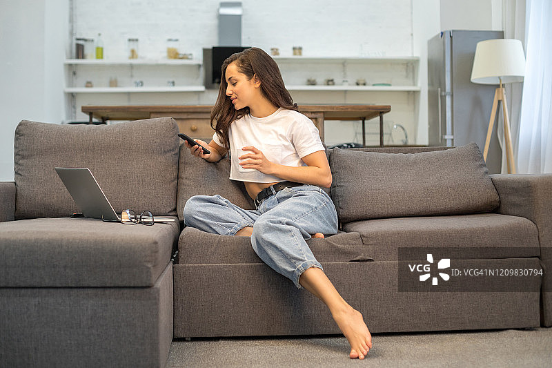 微笑的可爱女士在客厅里休息，手里拿着一杯咖啡图片素材