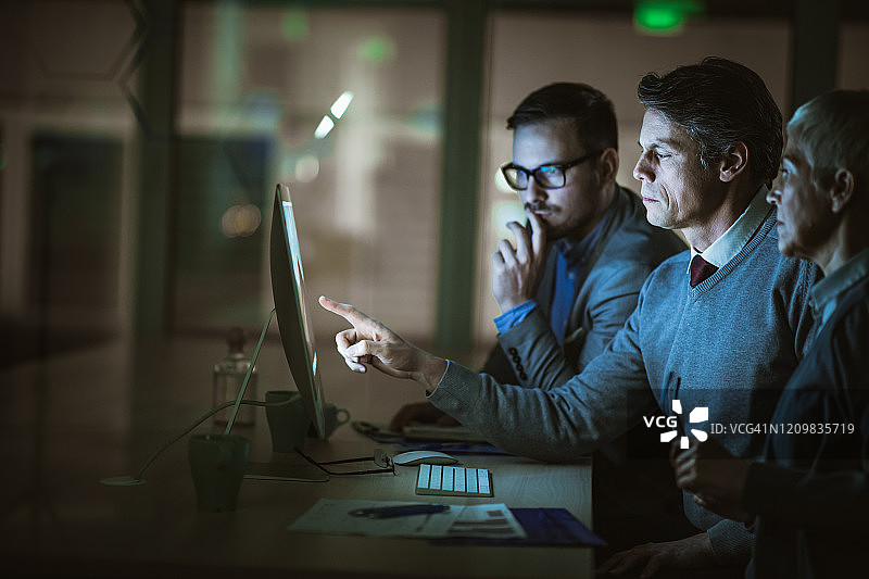 商务人士在昏暗的办公室分析台式电脑上的计划图片素材