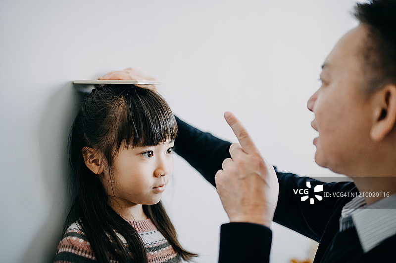 快乐的爷爷在客厅墙上测量孙女身高图片素材