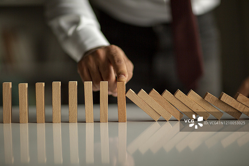 商人阻止多米诺骨牌效应：风险管理和保险概念图片素材