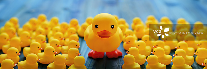 一只大型黄色鸭子站在绿松石色的木板桌子上，周围环绕着一大群黄色小橡皮鸭，寓意脱颖而出图片素材