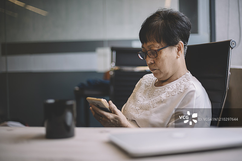 工作中休息看手机的亚洲老年妇女图片素材