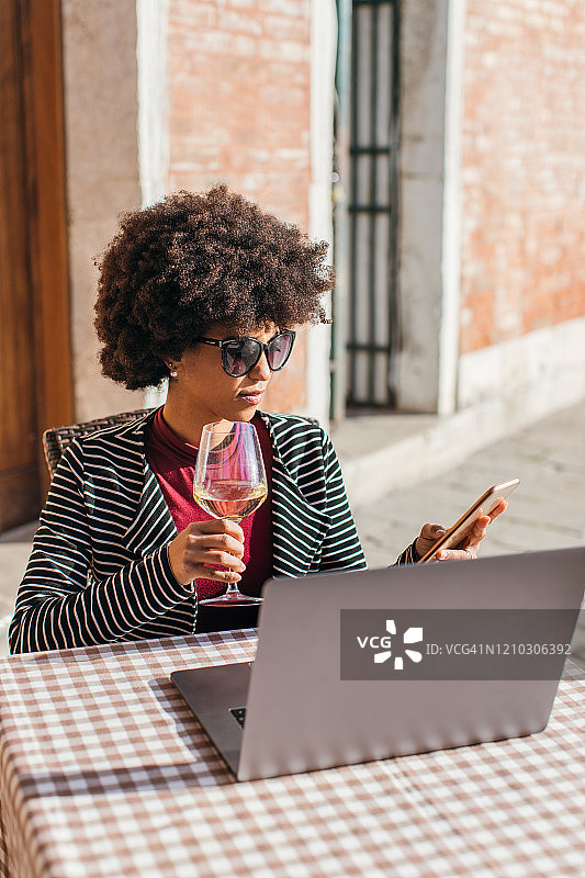 年轻的自由职业女性用手机喝葡萄酒图片素材