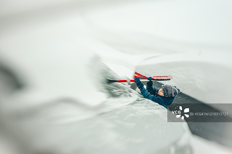 7岁男孩在暴风雪中清除汽车上的积雪图片素材