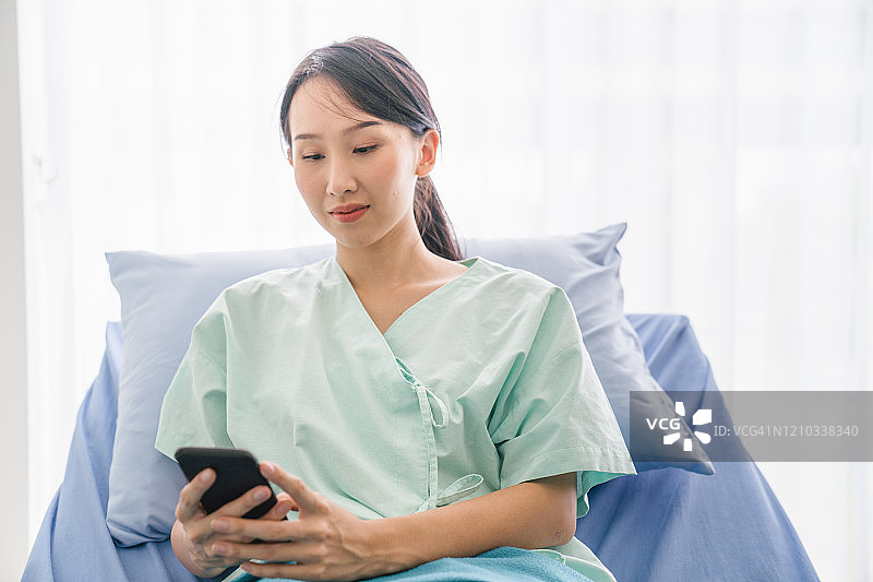 亚洲快乐的生病女性患者躺在医院病床上使用智能手机放松图片素材