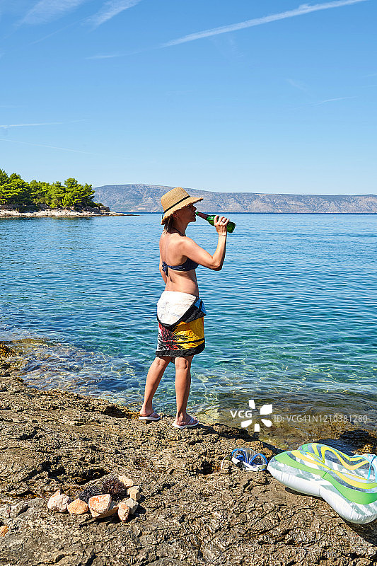 成年女人在克罗地亚耶尔萨的夏季假日中在蓝色大海边喝啤酒图片素材
