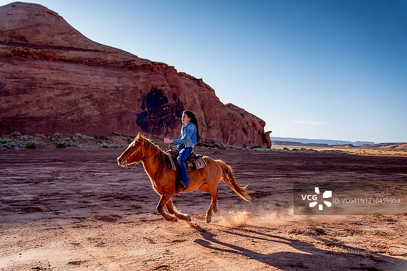年轻的纳瓦霍族少女骑马飞奔，小狗在后面追赶图片素材