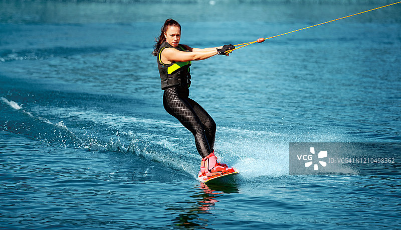 穿着潜水服熟练地玩尾波滑板的年轻女人图片素材
