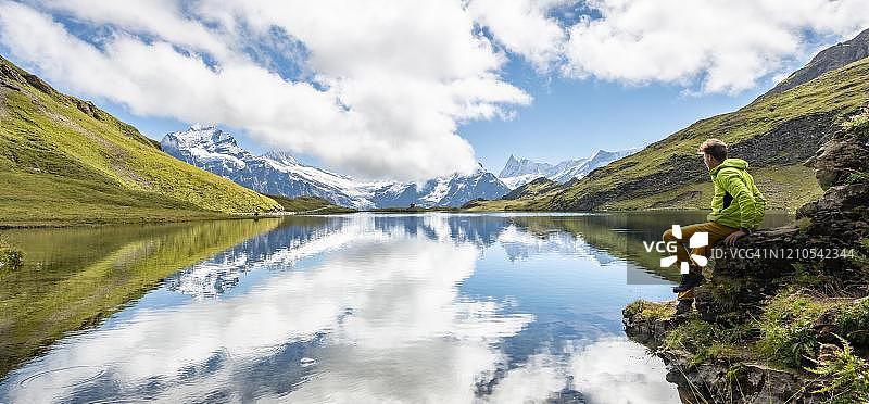 徒步旅行者坐在石头上,背景是巴赫阿尔普湖和施雷克峰和芬斯特拉尔峰,位于瑞士伯尔尼高地的格林德瓦图片素材