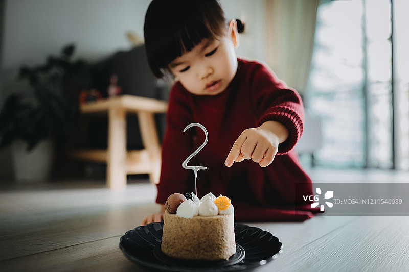 在家庆祝两岁生日，手捧生日蛋糕的可爱小女孩肖像照图片素材