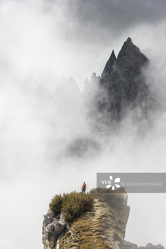 登山者站在山脊上,背后是山峰和尖锐的岩石,壮观的云彩,位于意大利贝卢诺奥龙佐迪卡多雷图片素材