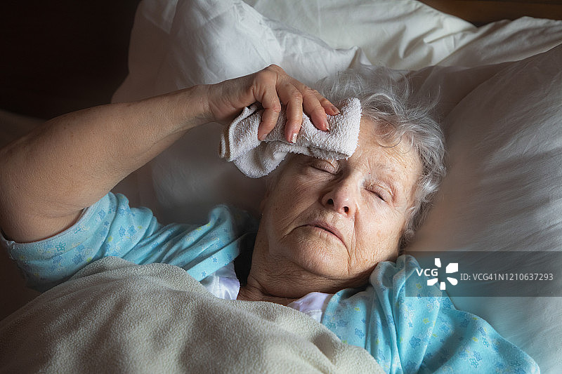 在床上用湿毛巾降温的生病老年女性图片素材