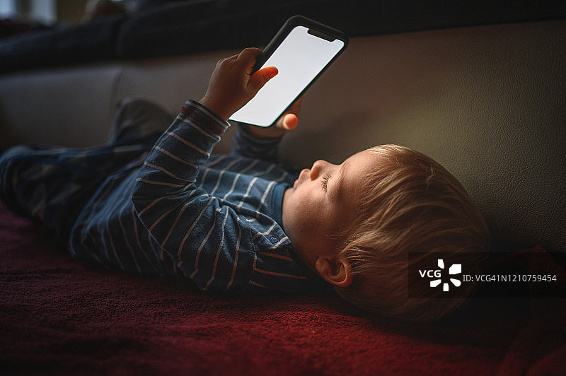 可爱的男孩拿着手机，仰卧在地板上图片素材