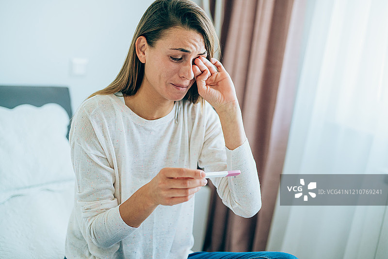 在家中拿着孕检棒的悲伤的年轻女人图片素材