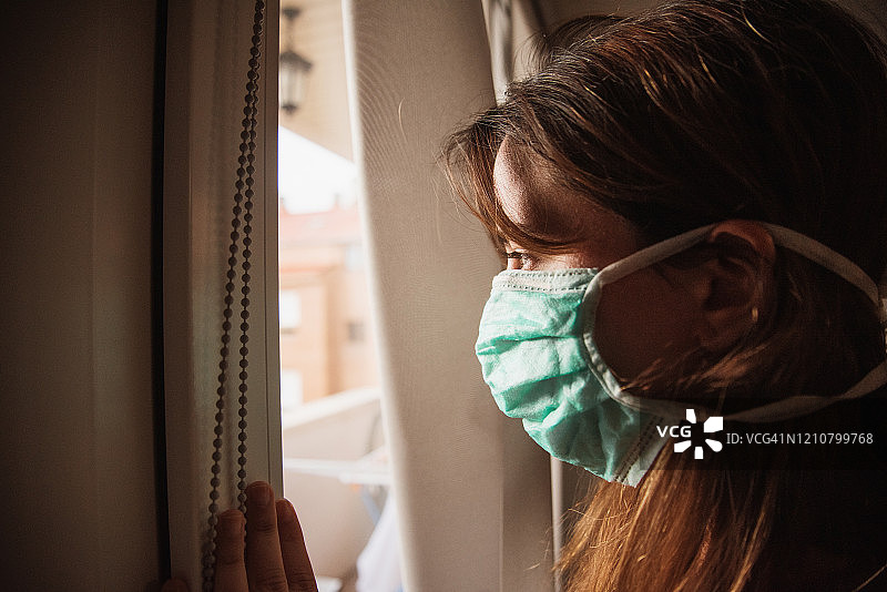 隔离期间戴着口罩看窗外的年轻女人图片素材