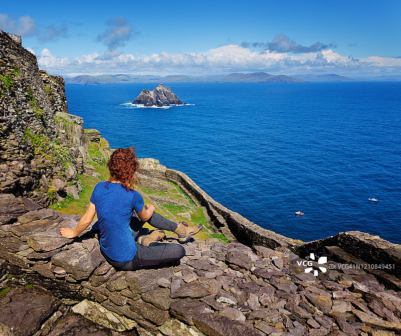 春天下午，坐在斯凯利格岛石墙上，背景是小斯凯利格岛的女人背影图片素材