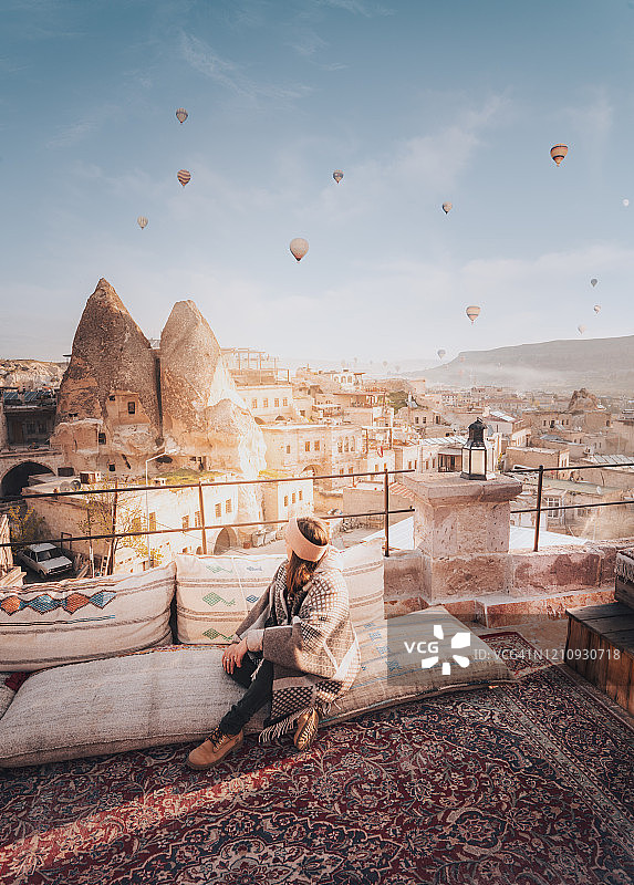 日出时分在土耳其卡帕多奇亚屋顶上的女人，背景是热气球图片素材