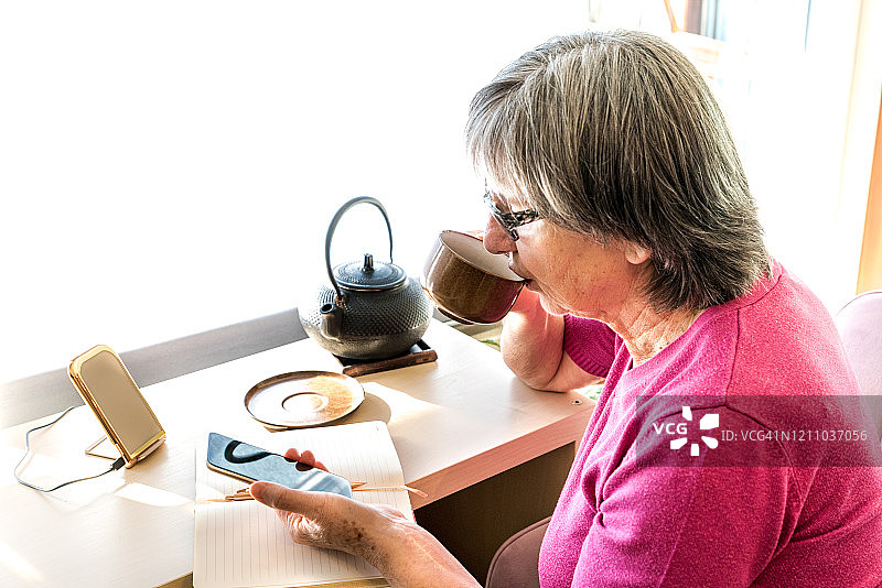 年长的女人在家使用手机和充电宝图片素材