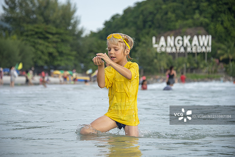 在马来西亚兰卡威海滩上手握湿沙的男孩图片素材