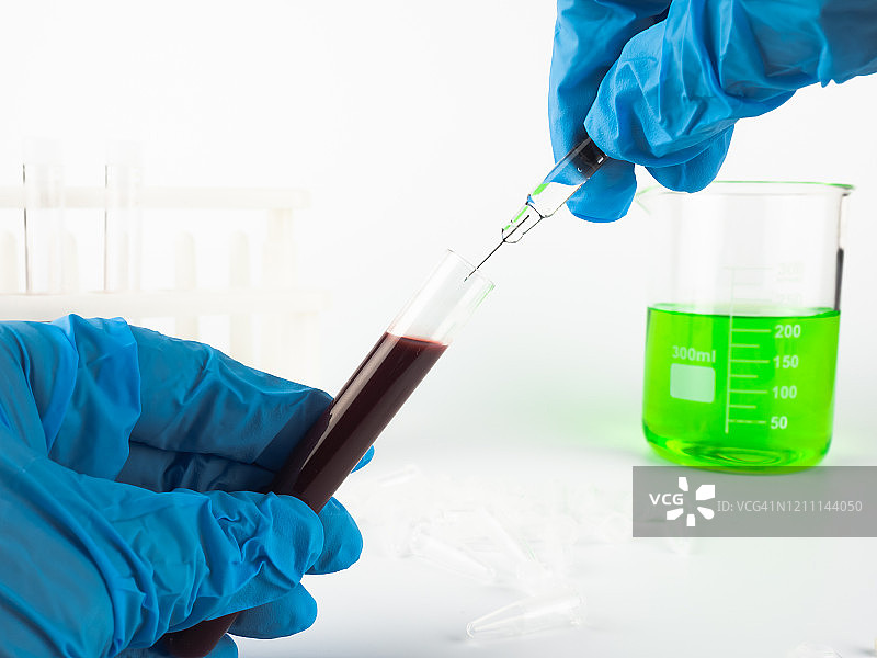 医生或科学家用注射器采集样本，放入实验室的试管中，试管中有血液样本和实验用玻璃器皿图片素材
